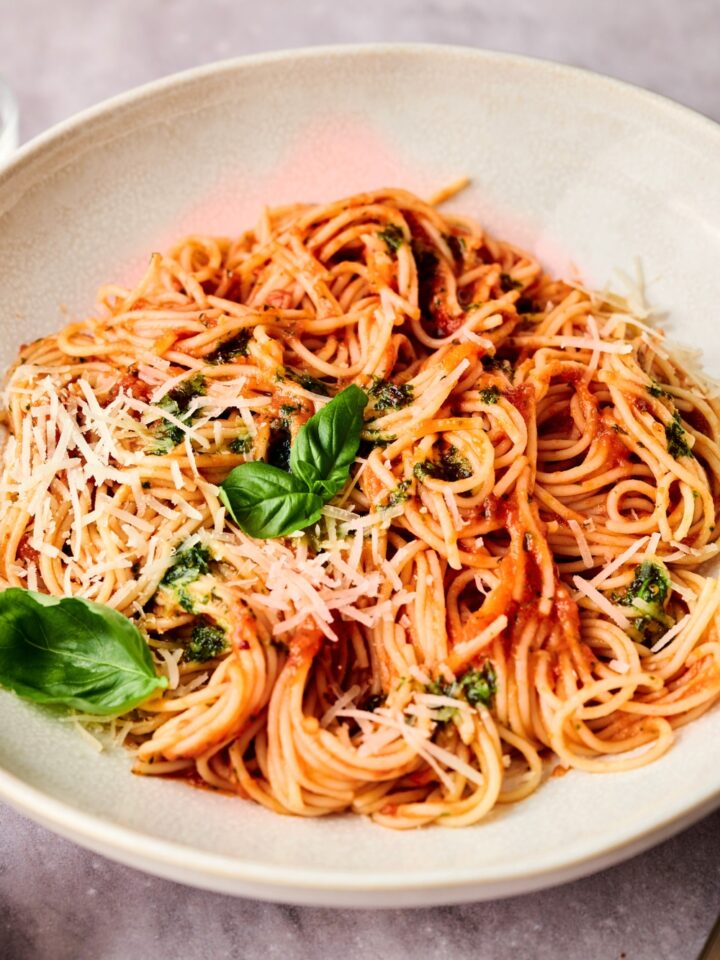 Spaghetti mixed in sauce with parmesan cheese and basil leaves on top.