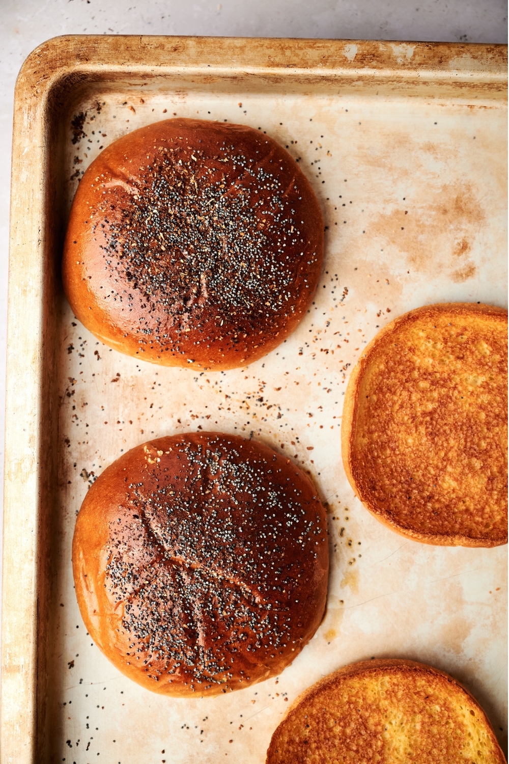 A baking sheet with toasted buns with sesame seeds and onions.