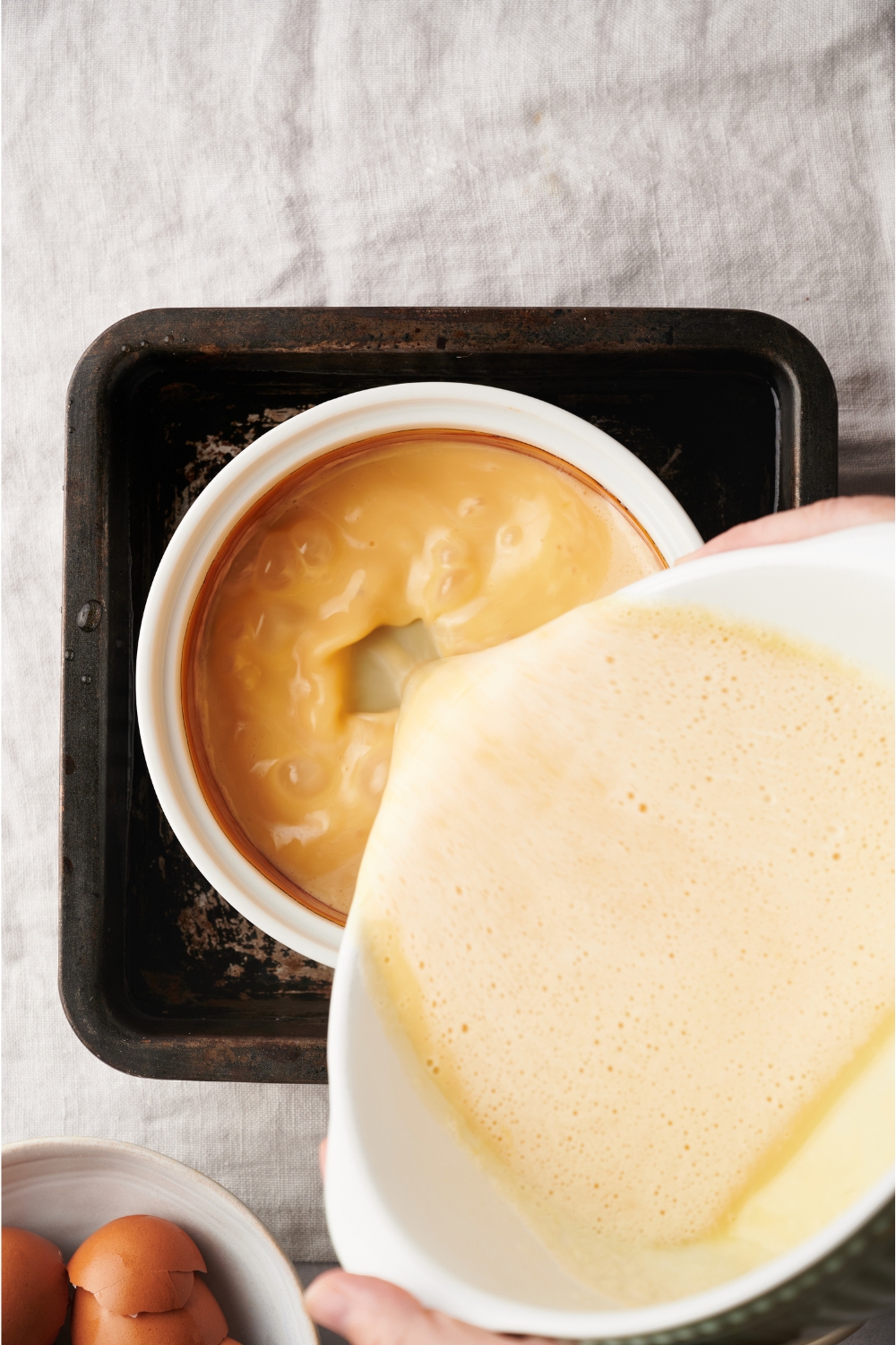 A baking pan with a water bath and a smaller round pan with flan batter in it.