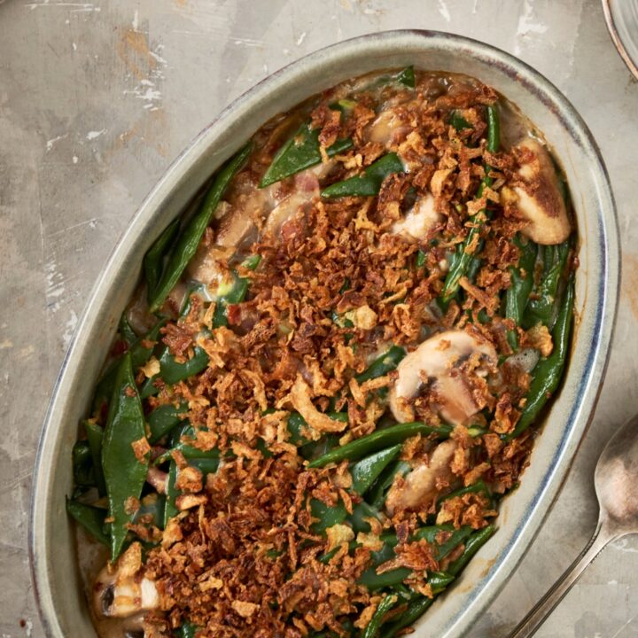 French fried onions on top of green beans and mushrooms in an oval casserole dish on top of a grey counter.