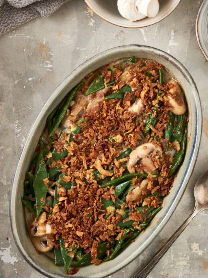 French fried onions on top of green beans and mushrooms in an oval casserole dish on top of a grey counter.