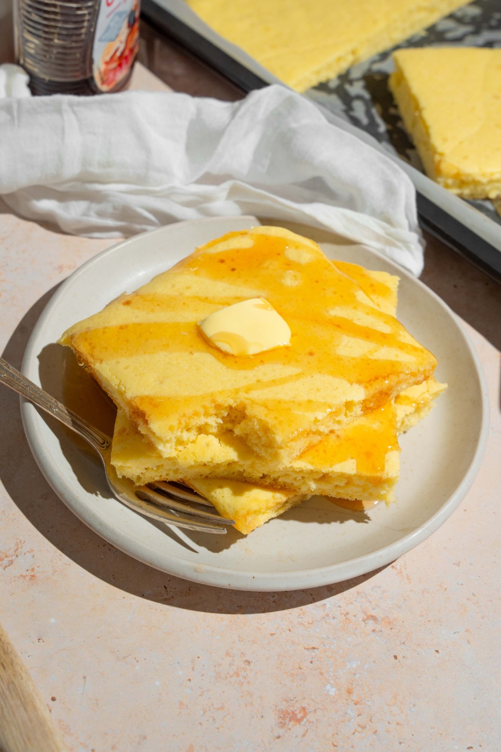 Three squares of sheet pan pancakes, stacked on top of one another on a white plate.