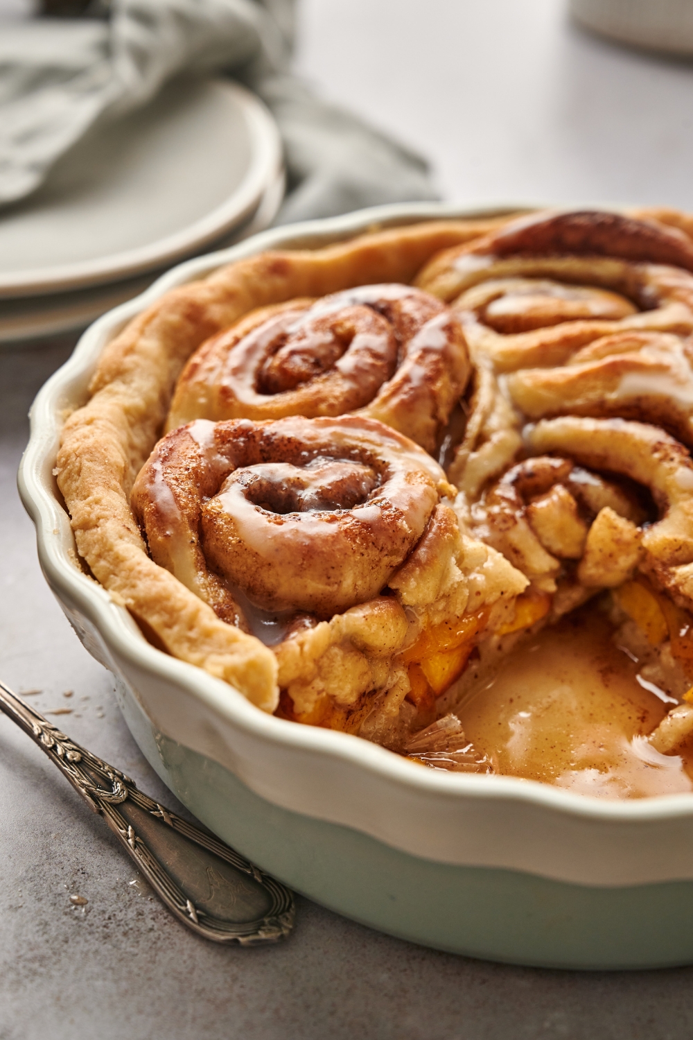 A pie dish with cinnamon roll peach cobbler with a slice taken out of it.