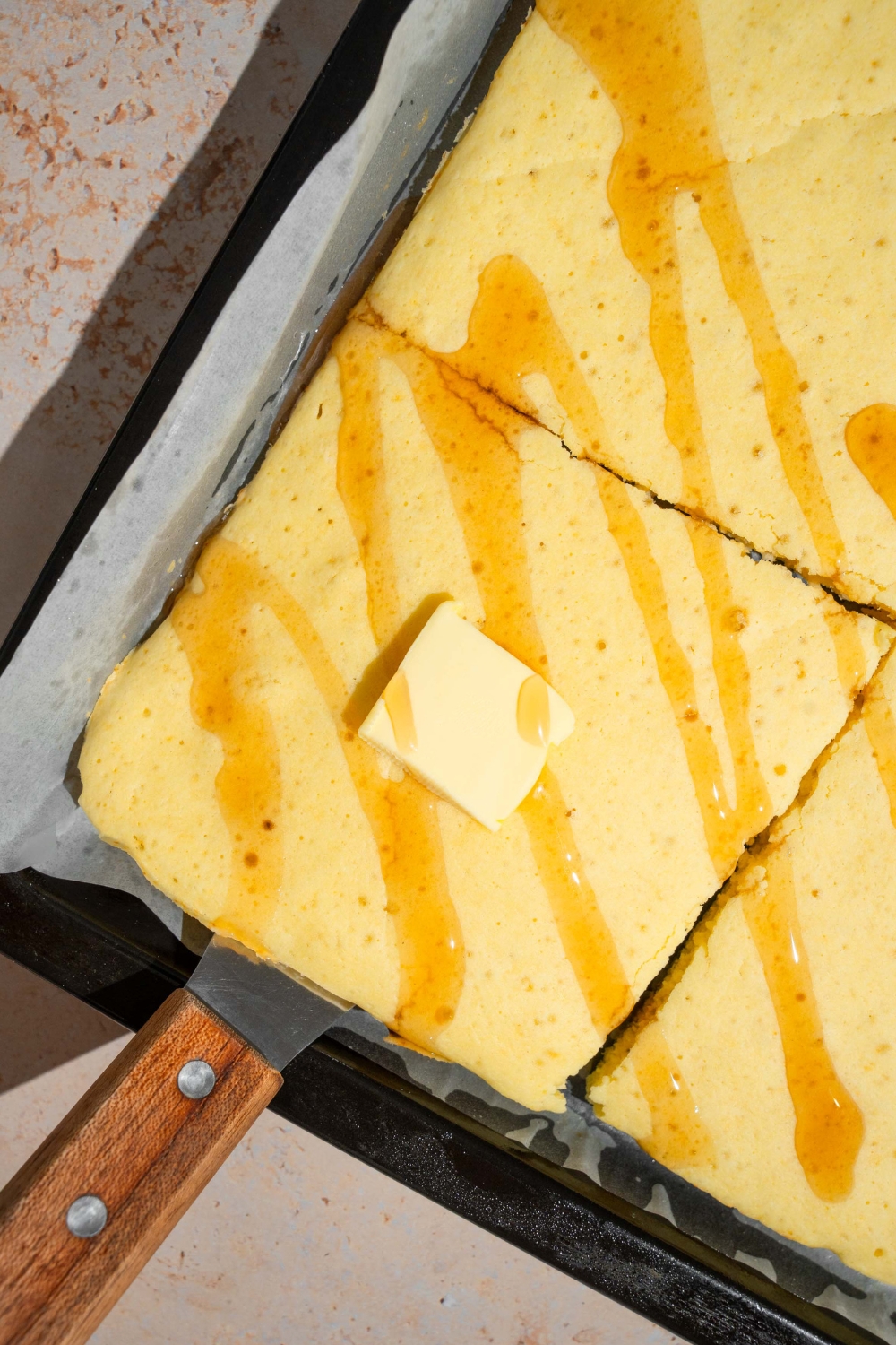 A pat of butter on top of a square of a sheet pan, pancake on a piece of parchment paper on a baking sheet.