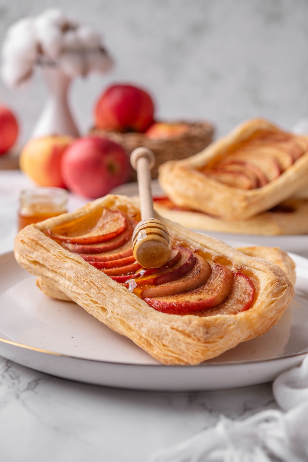 A honey dipper resting on top of an apple tart leaned on another tart on a plate.