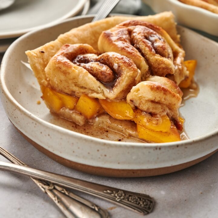 A serving dish with a slice of cinnamon roll peach cobbler.