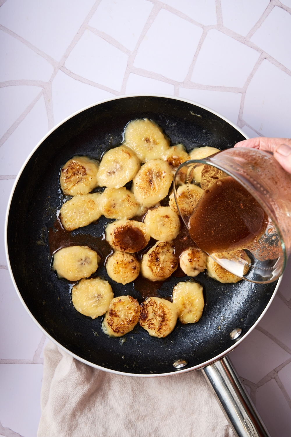 A frying pan with sliced bananas and the honey mixture being added to the slices.