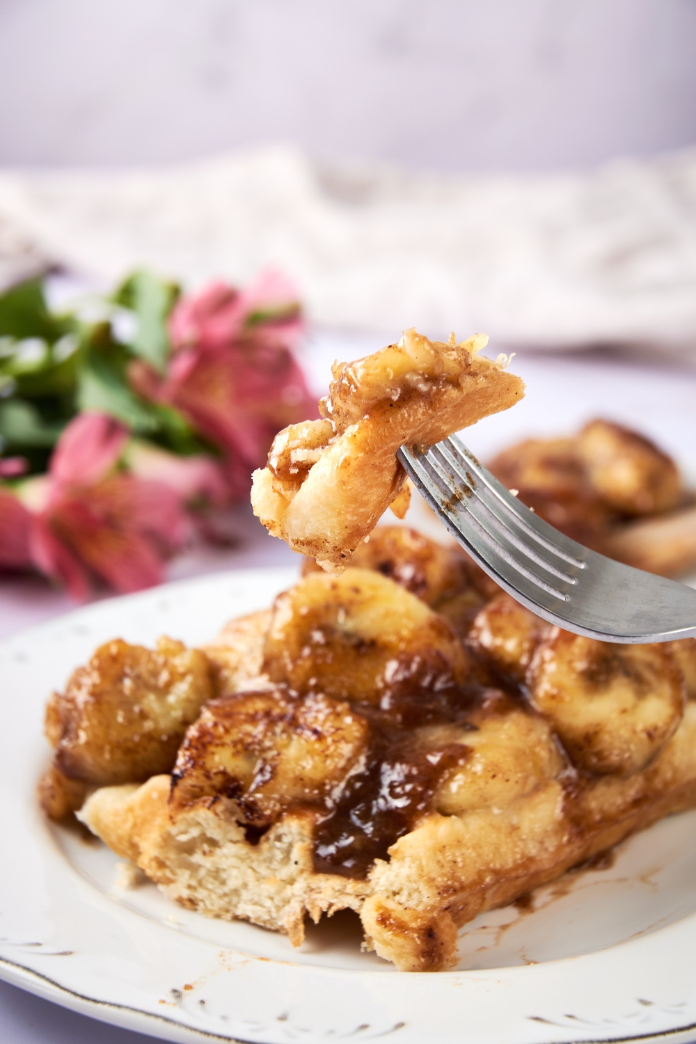 A plate with fried bananas served on top of a waffle. A fork is holding up a bite of fried bananas.