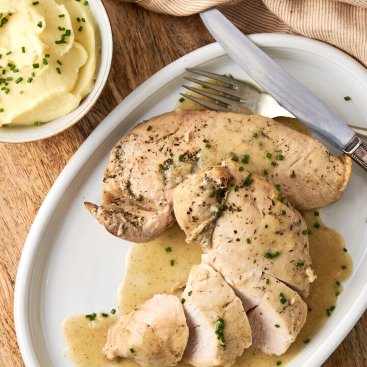 A serving tray with sliced tender turkey smothered in butter sauce. A side of mashed potatoes is in the background.