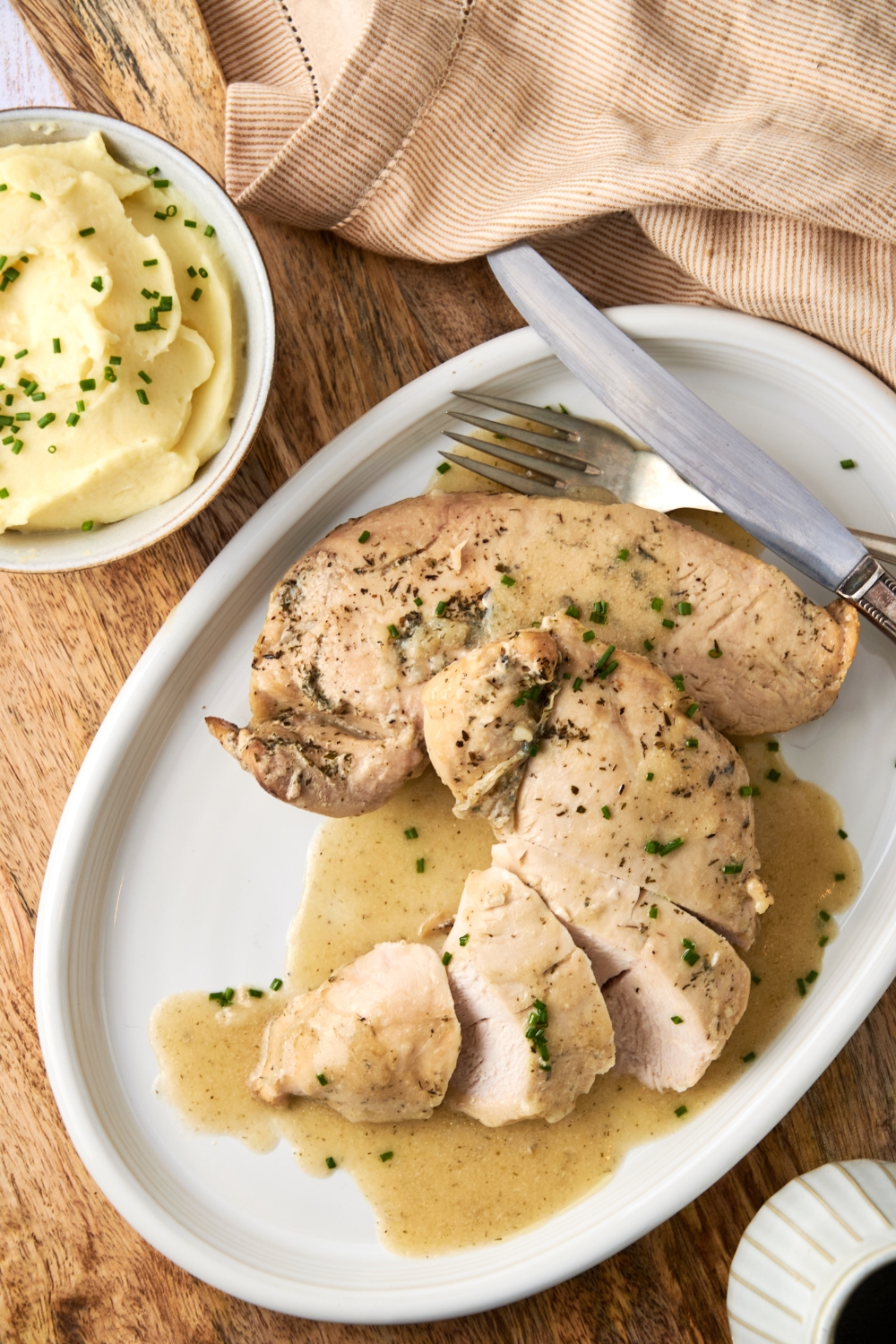 A serving tray with sliced tender turkey smothered in butter sauce. A side of mashed potatoes is in the background.