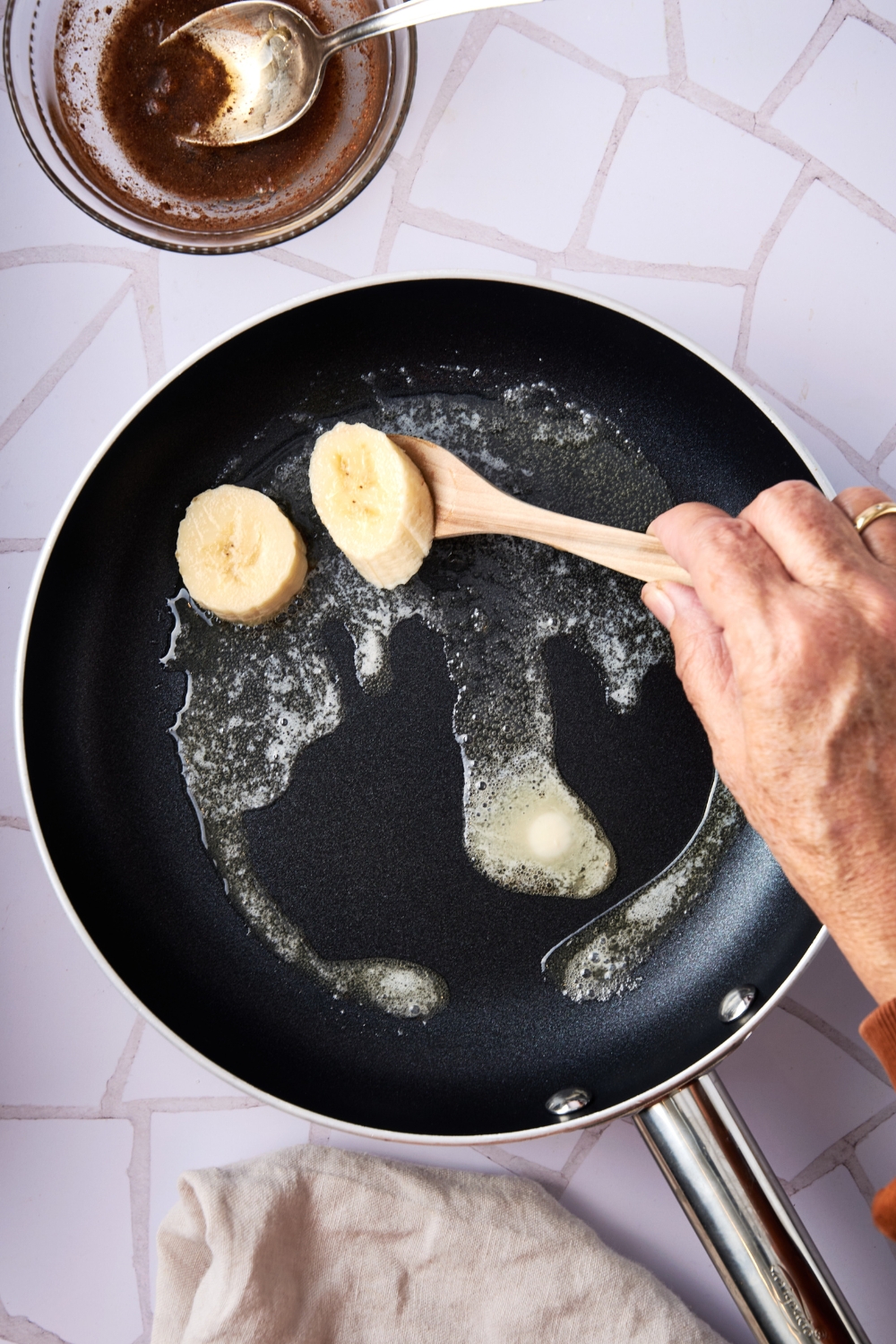 A frying pan with melted butter and banana slices being added to it.