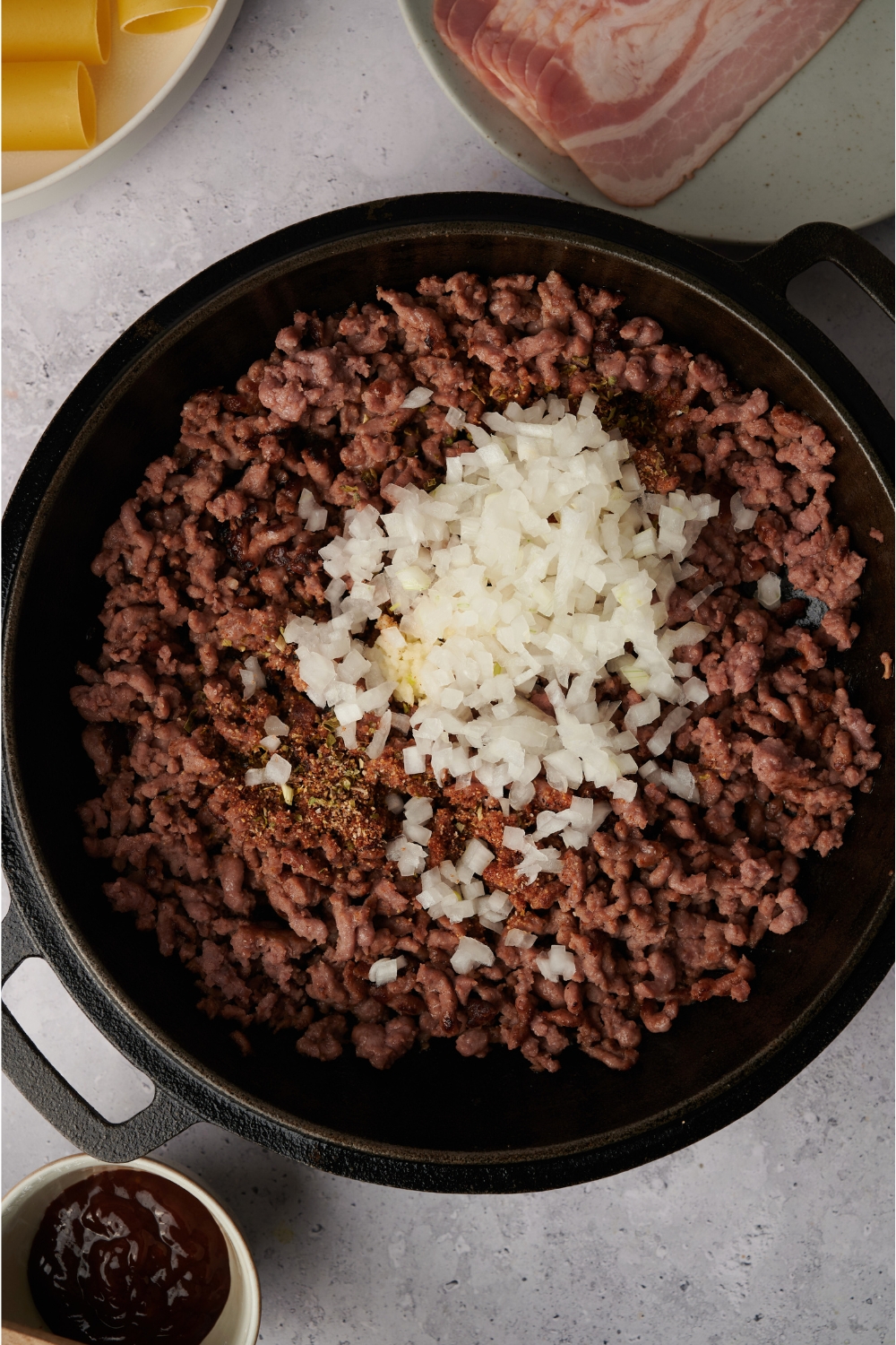 A skillet with ground beef cooking. Garlic, onions, and seasonings have just been added.