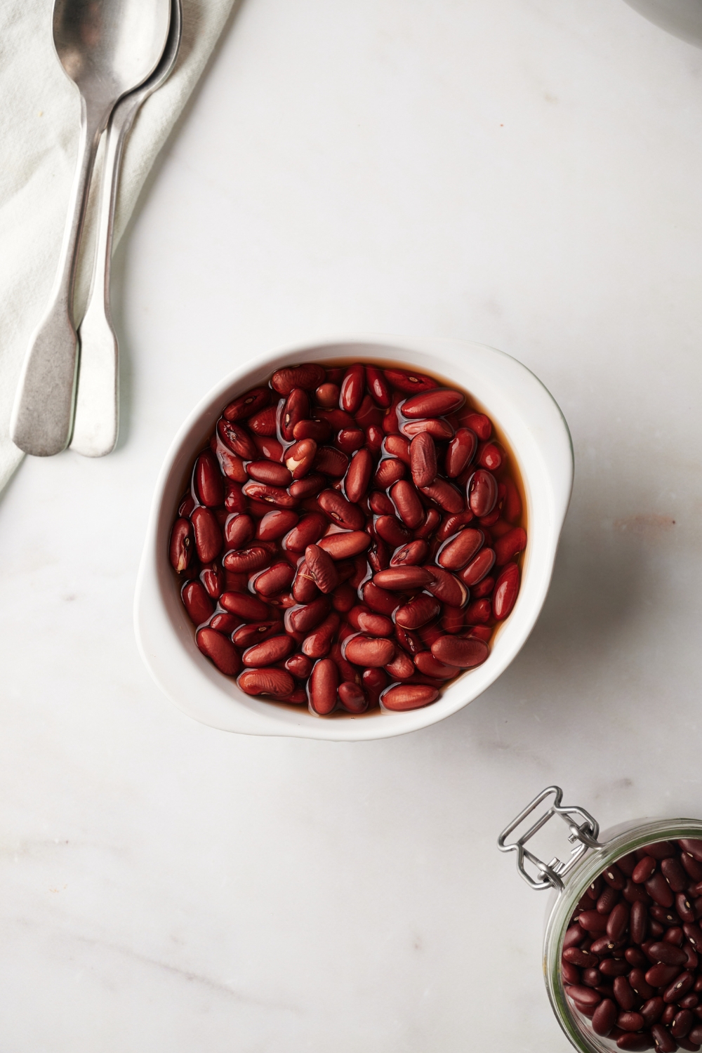 Kidney beans in a white bowl in water on a white counter.