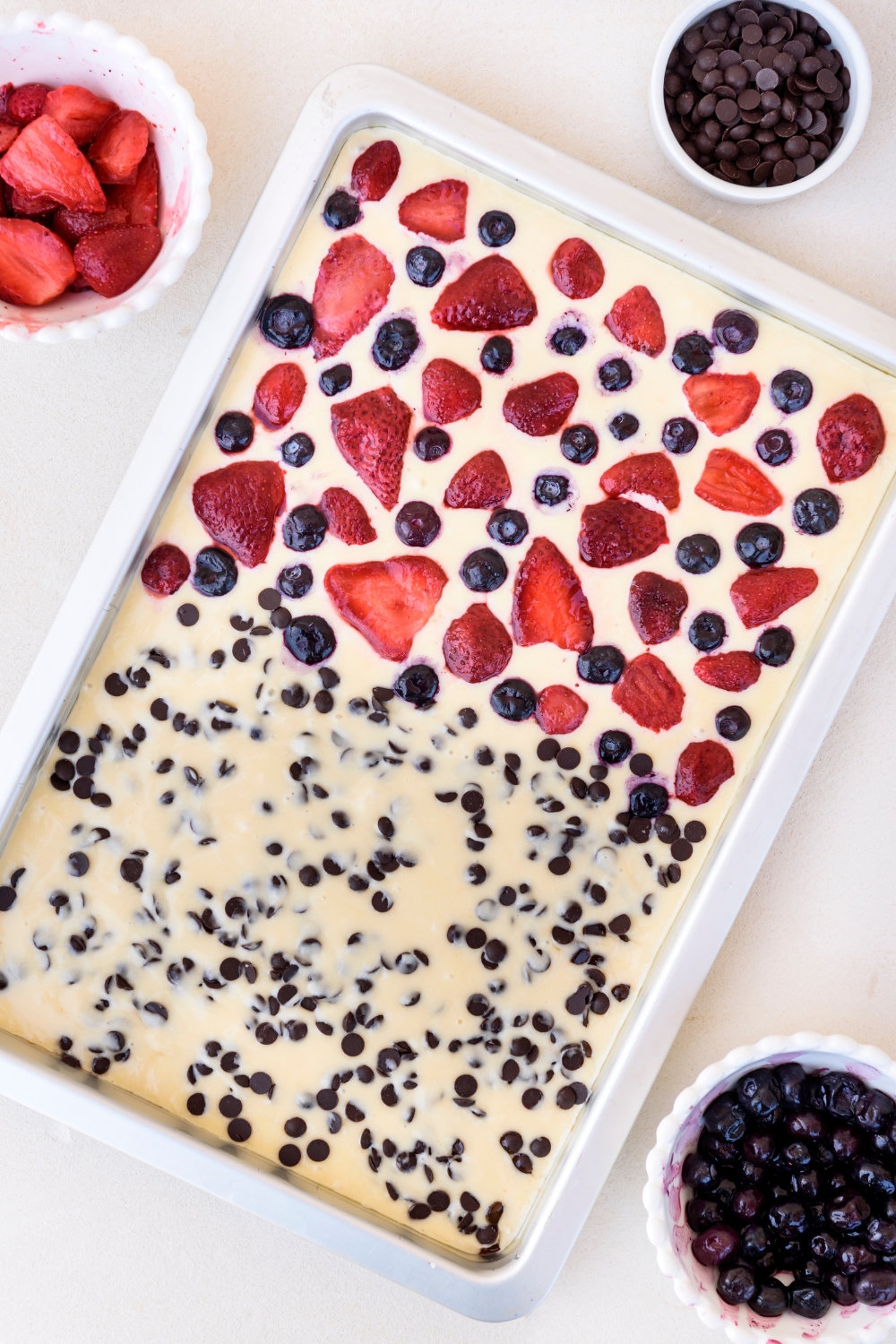 A baking sheet with pancake batter topped with strawberries, blueberries, and chocolate chips.strawberries, blueberries, and chocolate chips.