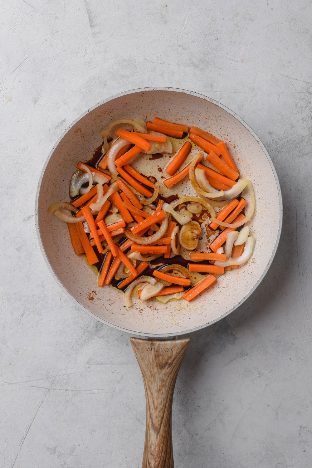 A frying pan with carrots and onions cooking.