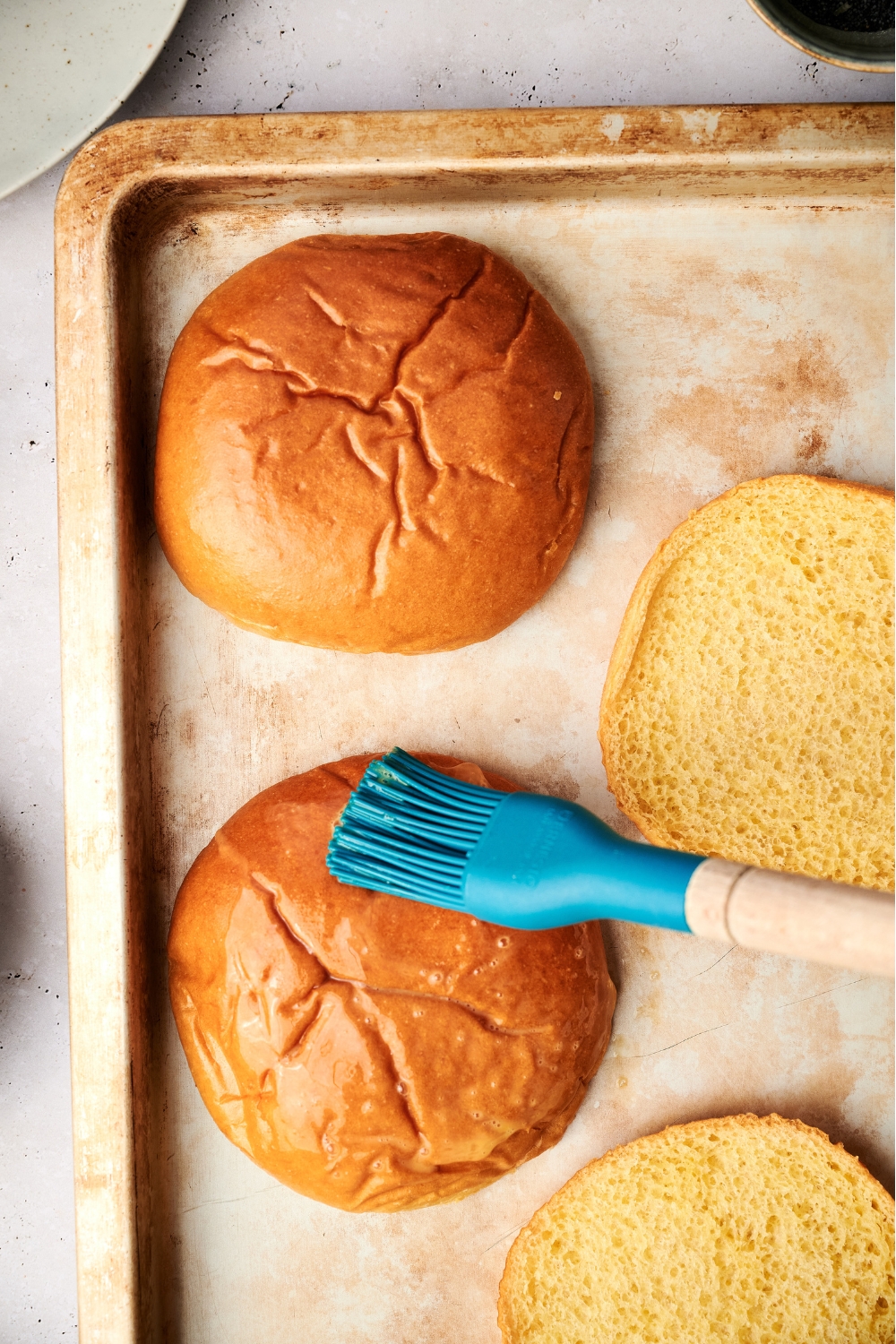 A baking sheet with burger buns being brushed with egg wash.