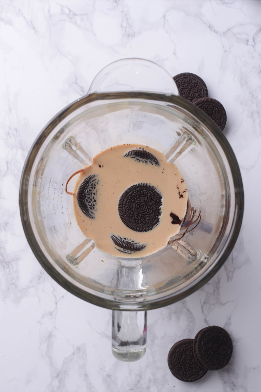 A blender with milk, oreo cookies, ice, and chocolate sauce in it.