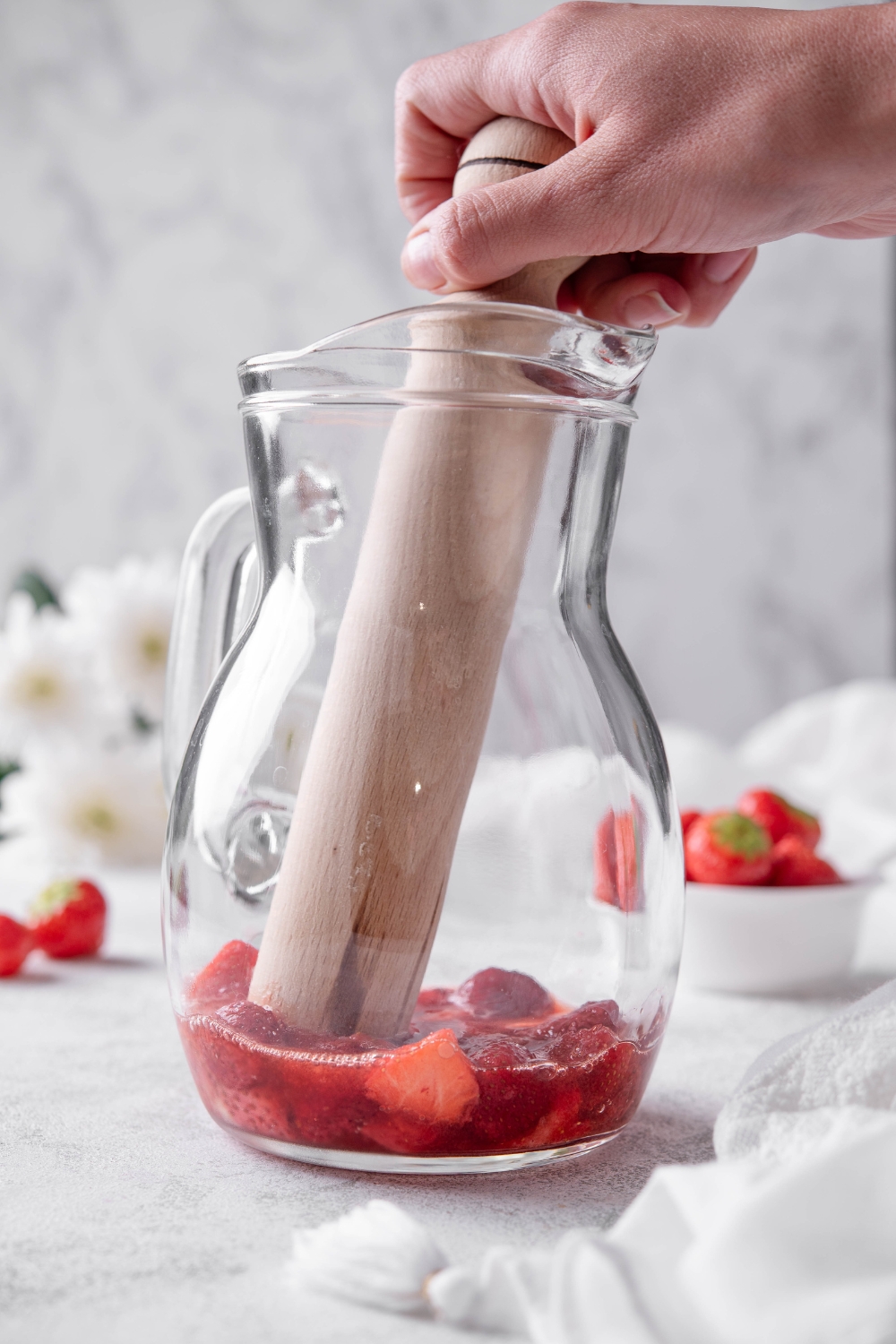 A pitcher with fresh strawberries being muddled.