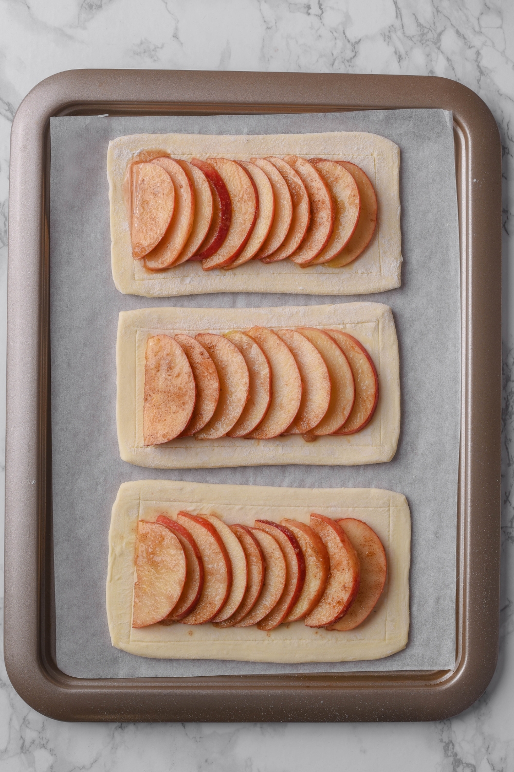 Puff pastry sheets topped with sliced apple tart filling on a parchment paper lined baking sheet.