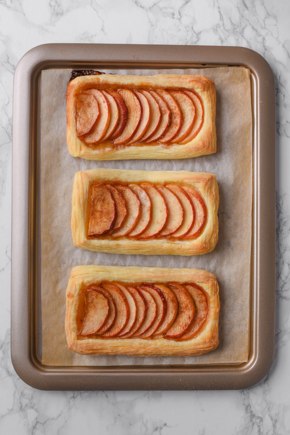 Three puff pastry apple tarts on a parchment paper lined baking sheet.