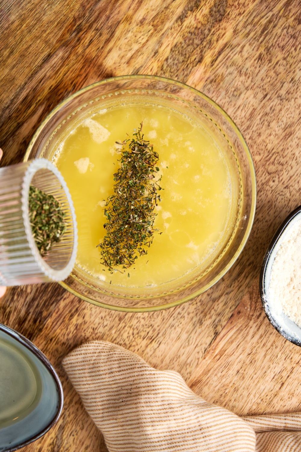 A small bowl with seasonings and herbs being added to the butter mixture.