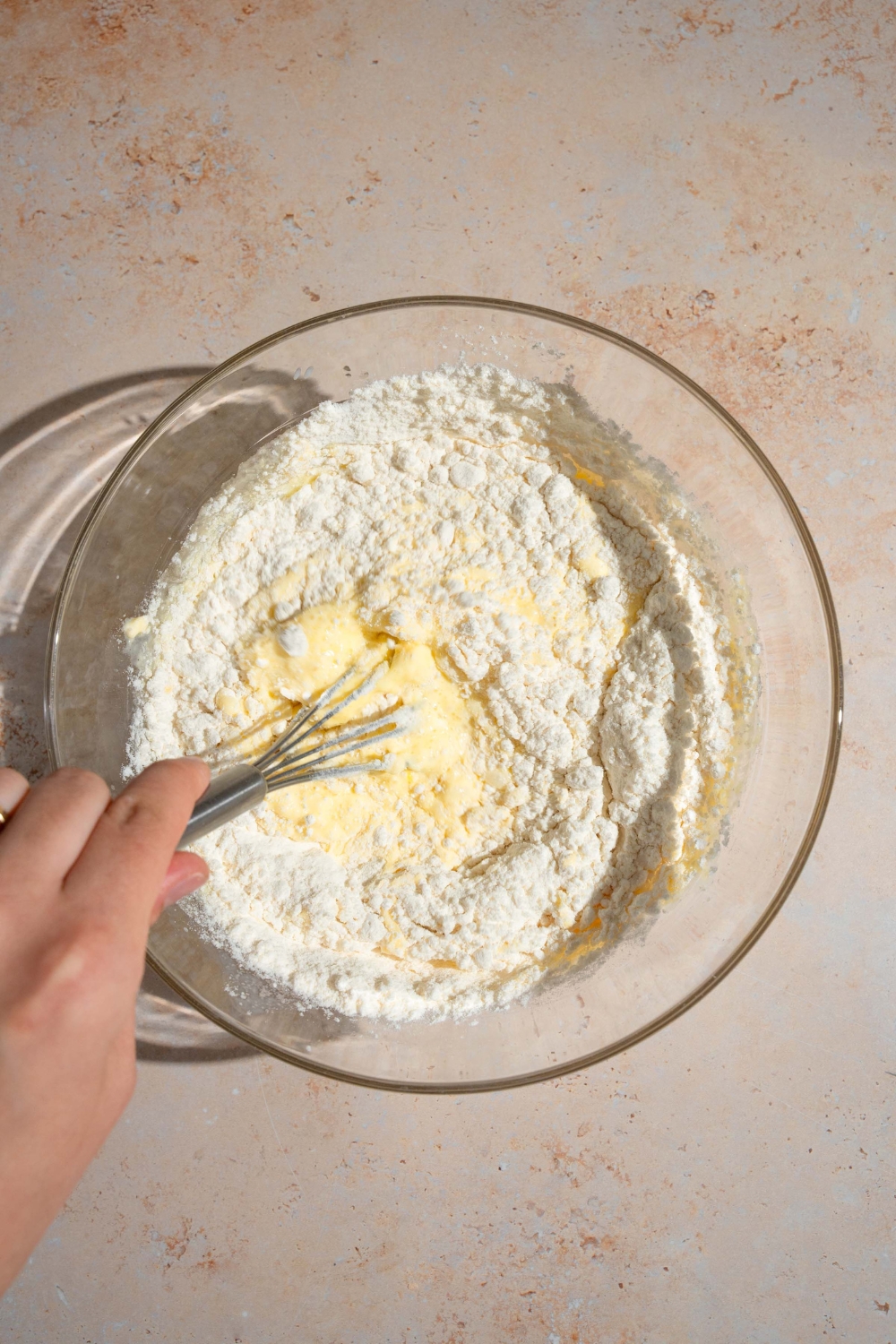 A hand whisking flour in a glass bowl.