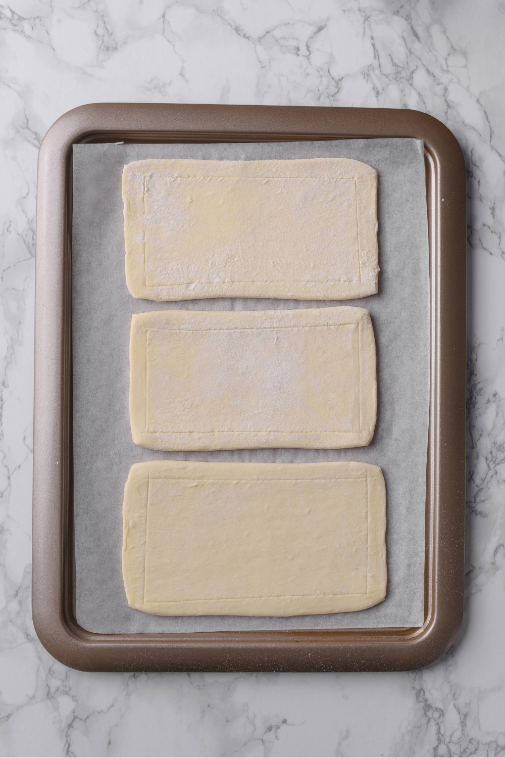Three rolled out puff pastry sheets on a parchment paper lined baking sheet.