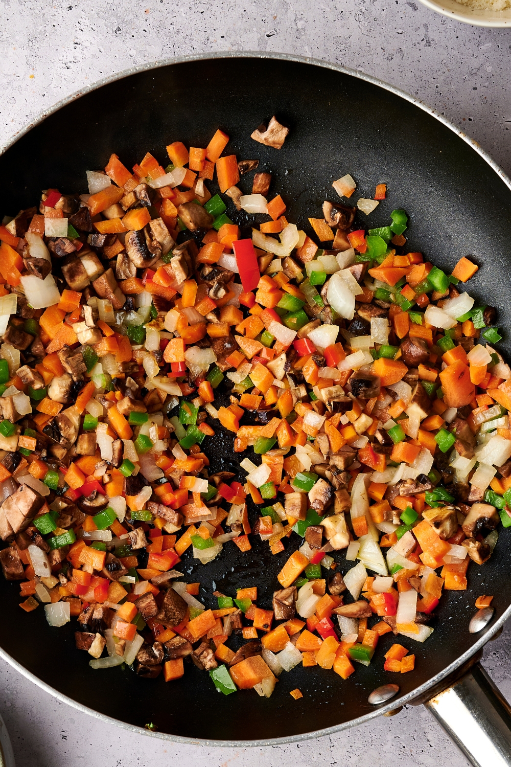 A skillet with cooked diced carrots, bell pepper, onion, and mushroom.