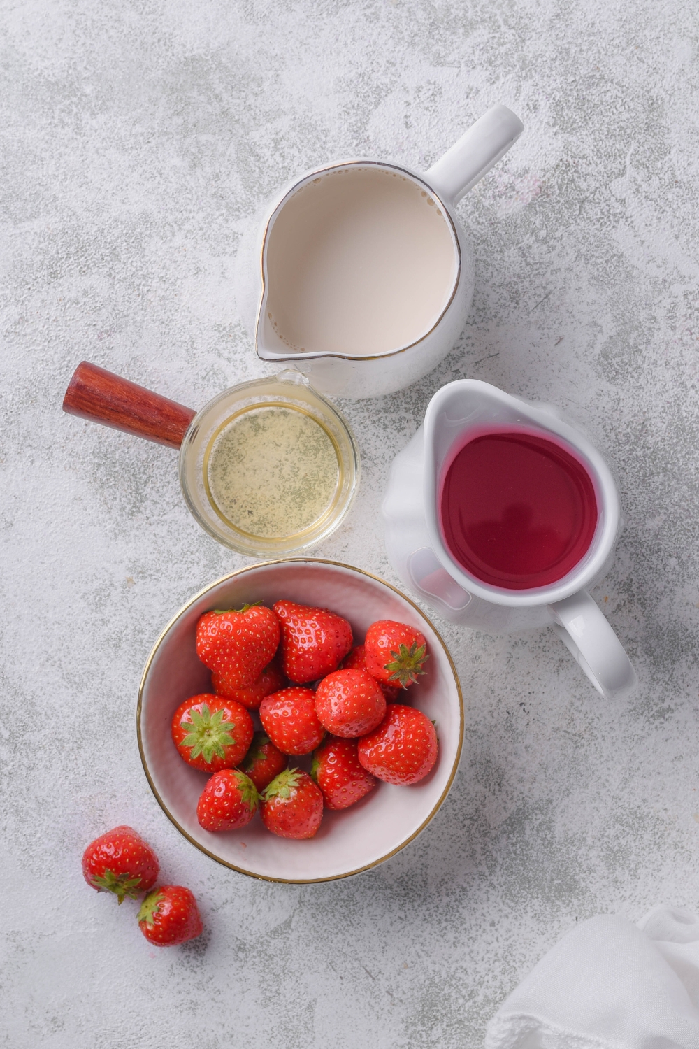 A countertop with a pitcher of white cran-strawberry juice, coconut milk, simple syrup, and fresh strawberries.