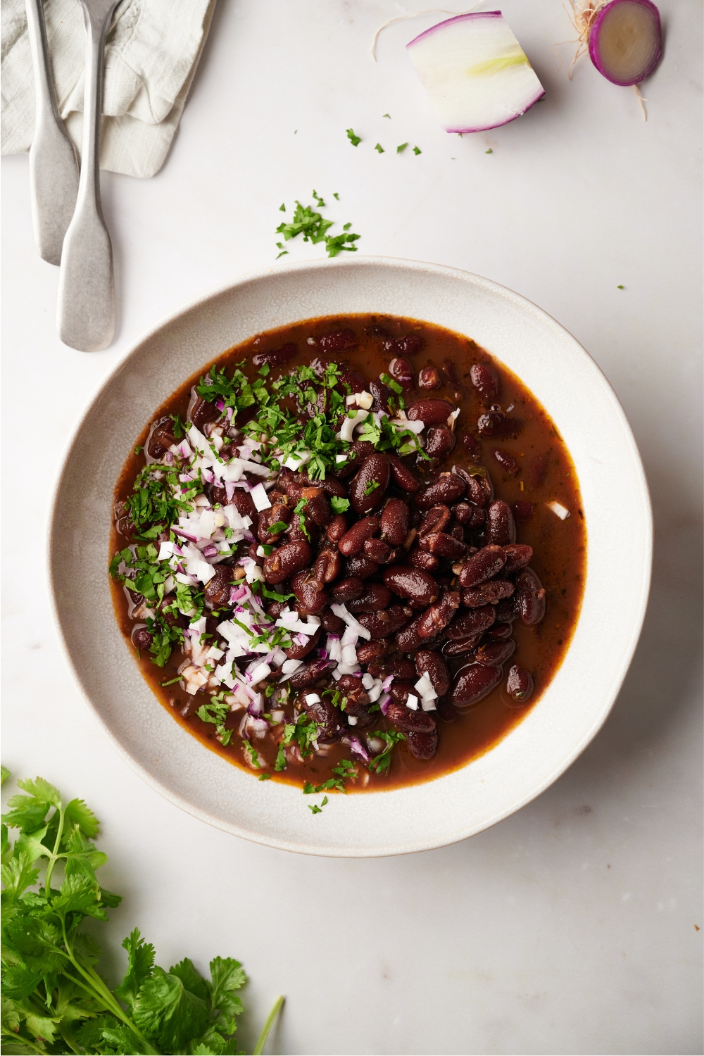 Red kidney beans, onions, and chives in a white bowl on a white counter.