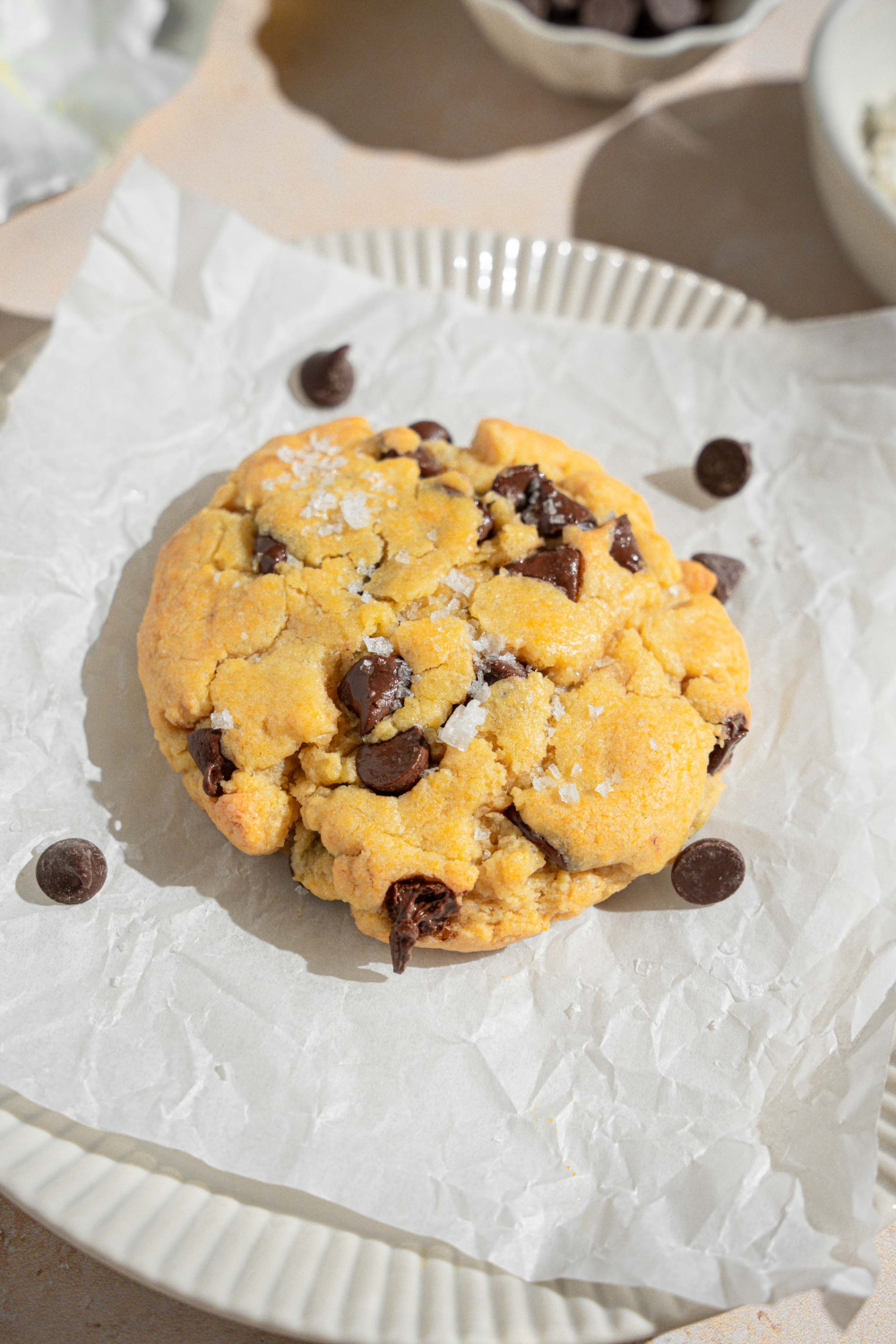 A chocolate chip cookie that is on a piece of parchment paper on a plate.