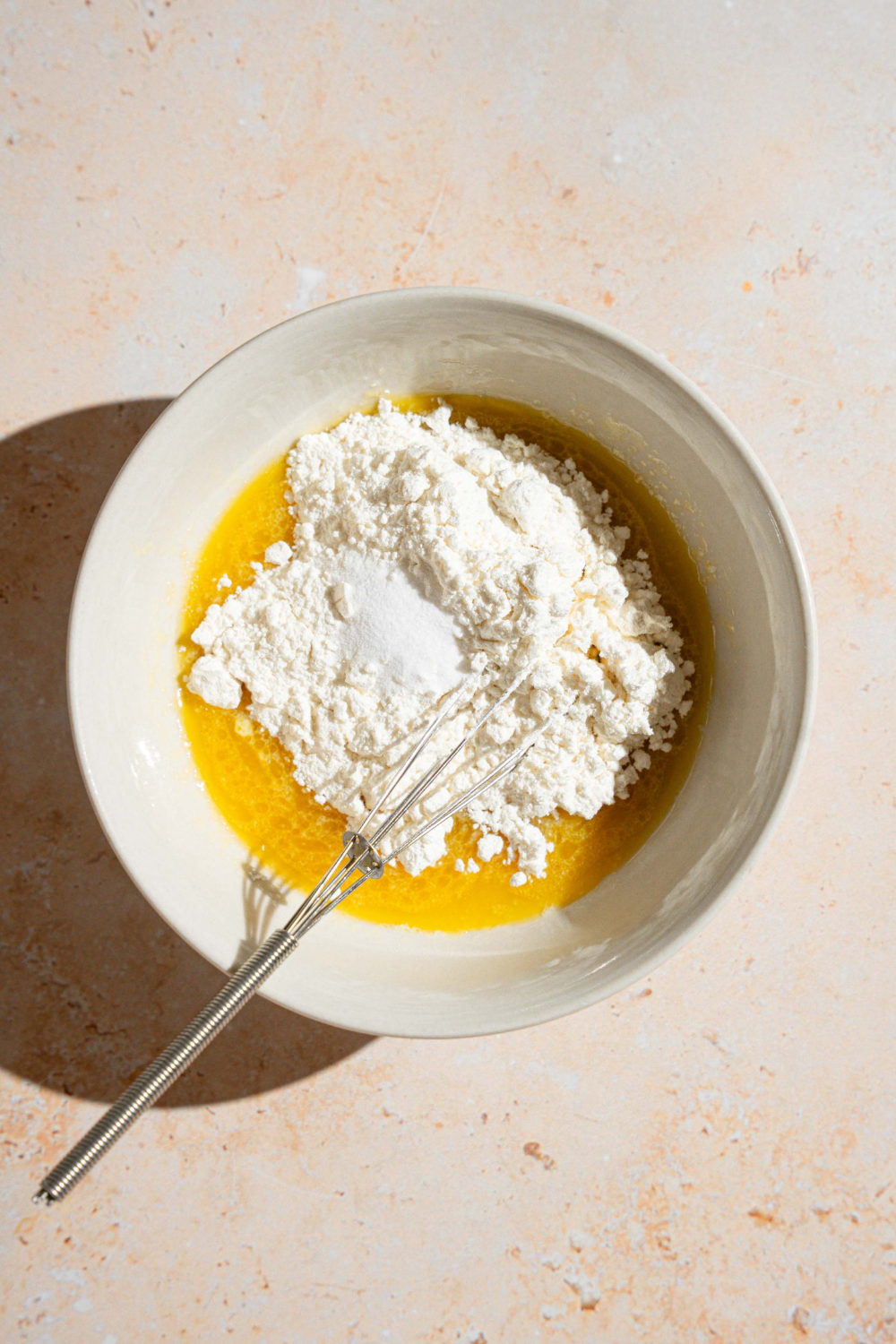 Flour on top of wet ingredients for cookie dough in a white bowl.