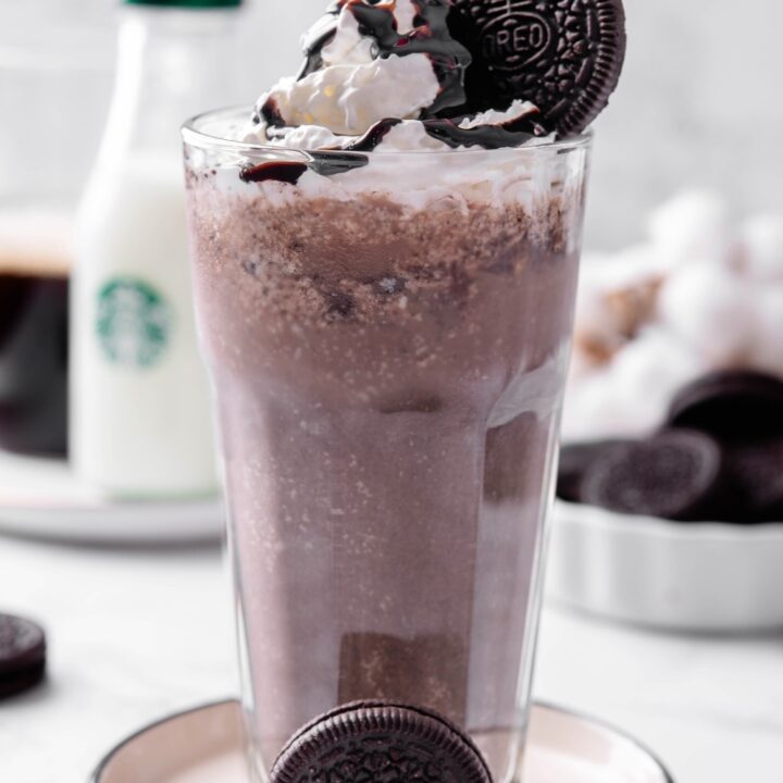 A mocha cookie crumble frappuccino in a tall glass with whipped cream, chocolate sauce, and an Oreo on top;