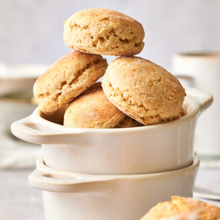 A biscuit stacked on top of two biscuits leaning against one another on more biscuits in a white bowl that is in another white bowl on a grey counter.