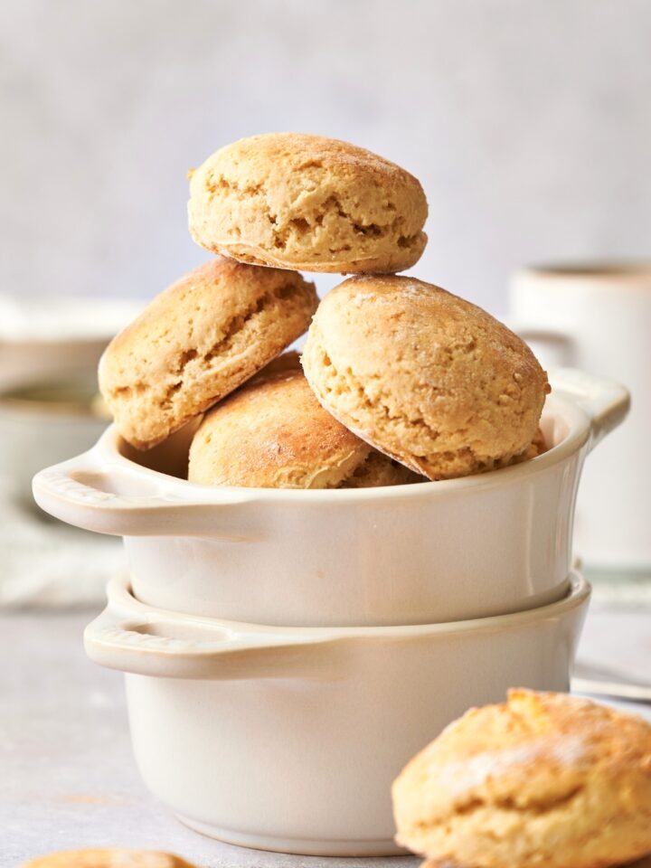 A biscuit stacked on top of two biscuits leaning against one another on more biscuits in a white bowl that is in another white bowl on a grey counter.