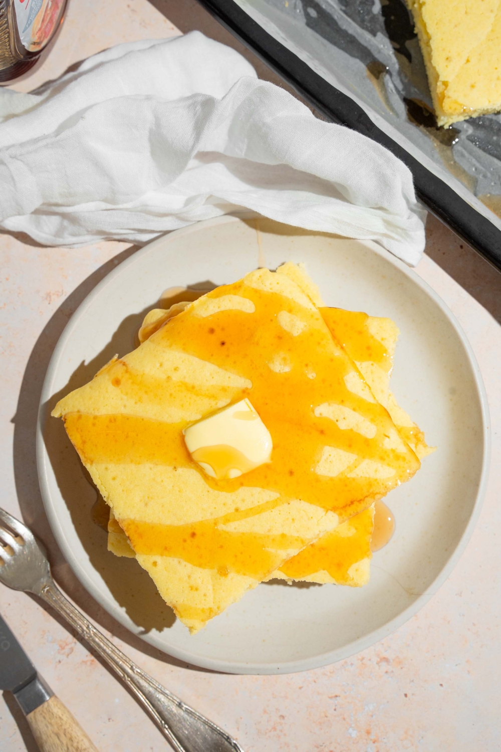 A couple squares of sheet pan pancakes, stacked on top of one another on a white plate.