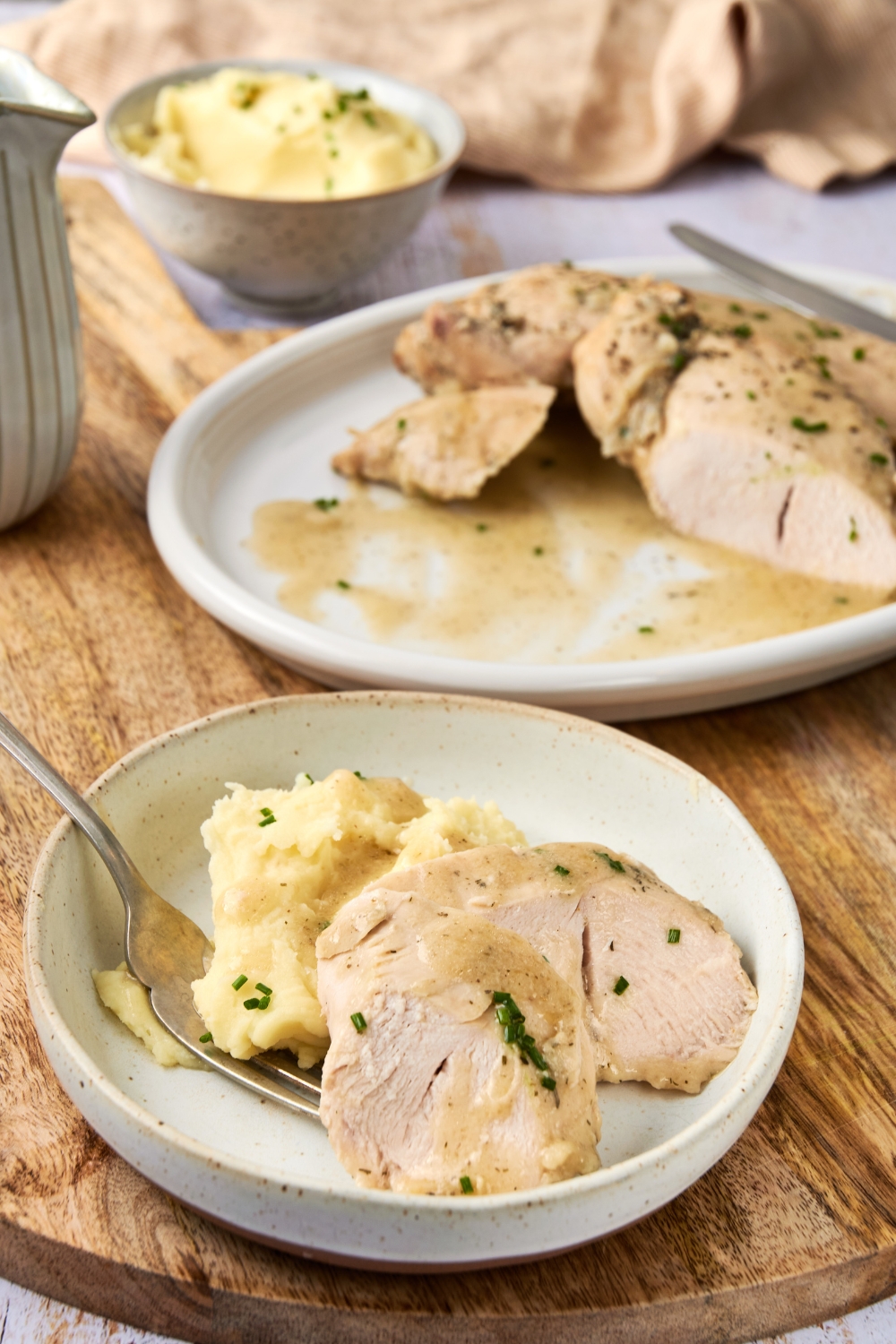 A plate with sliced tender turkey smothered in butter sauce and a side of mashed potatoes. The serving tray with the remaining breast is in the background.