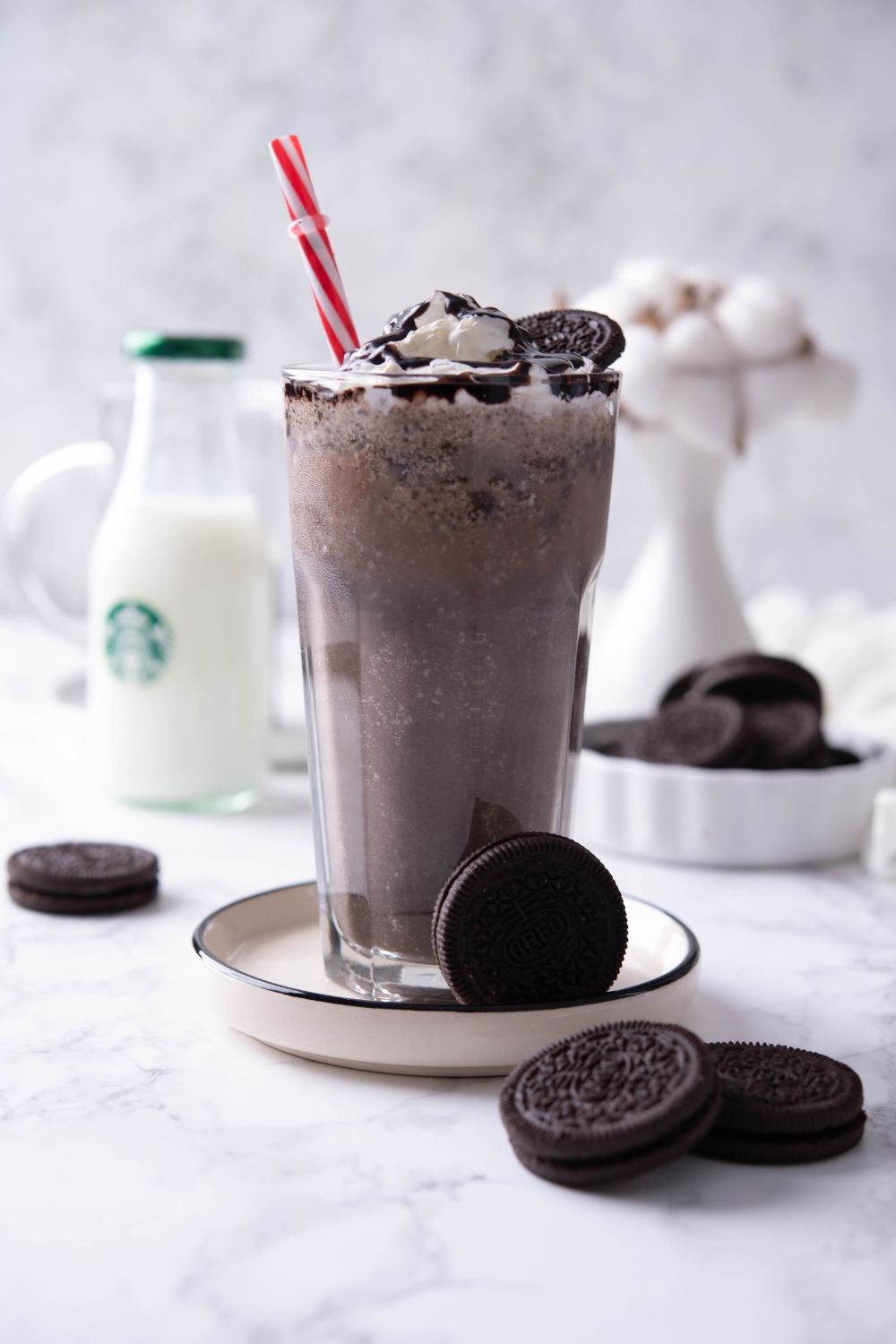 A tall glass with the Starbucks cookie crumble frappuccino topped with whipped cream, chocolate drizzle, and oreo cookies.