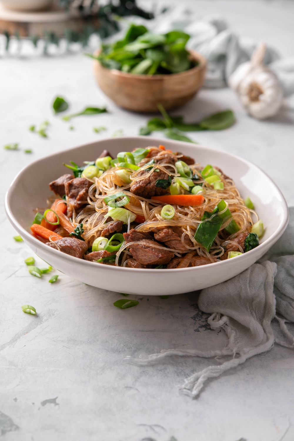 A bowl with glass noodles, beef cubes, green onions, and veggies.