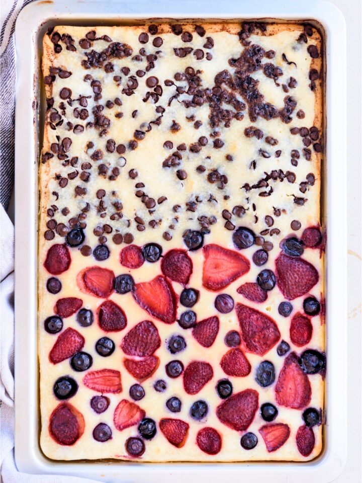 Pancakes in a sheet pan with chocolate chips on the top half and strawberries and blueberries on the bottom half.