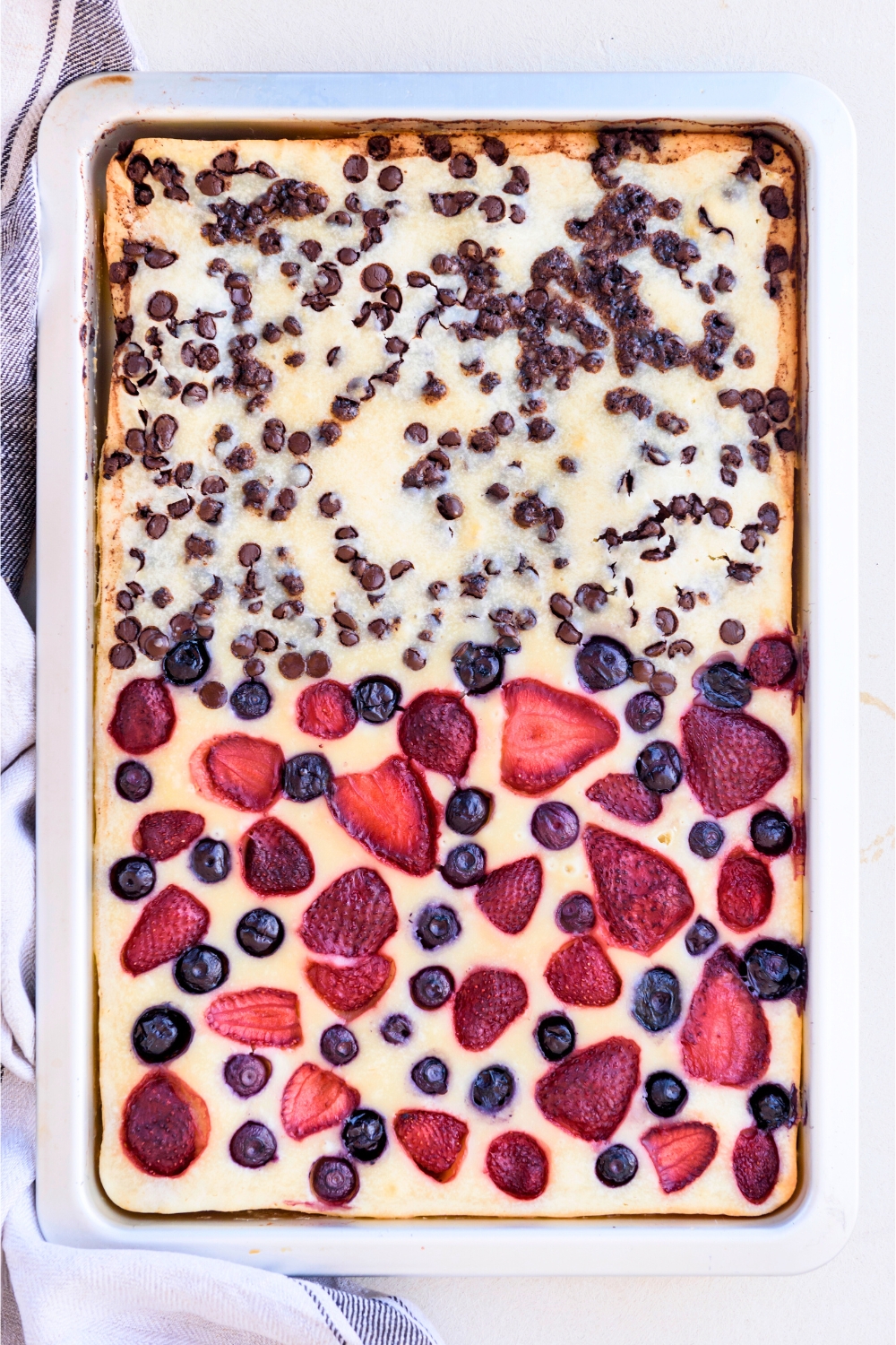 Pancakes in a sheet pan with chocolate chips on the top half and strawberries and blueberries on the bottom half.