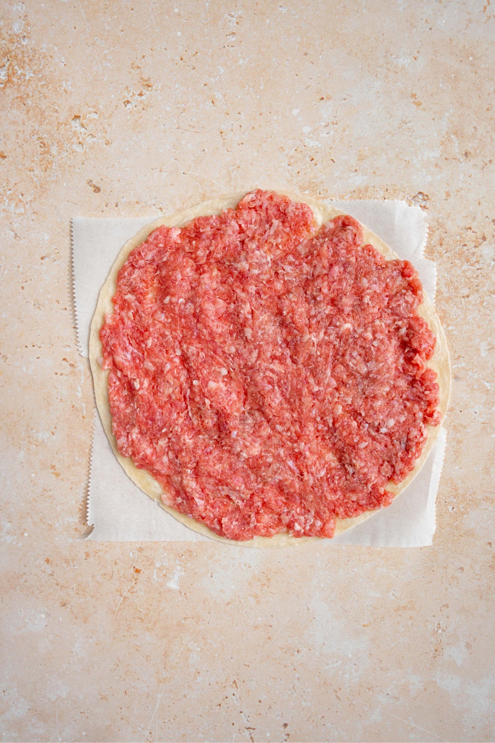 A smashed burger patty on a piece of parchment paper on a white counter.