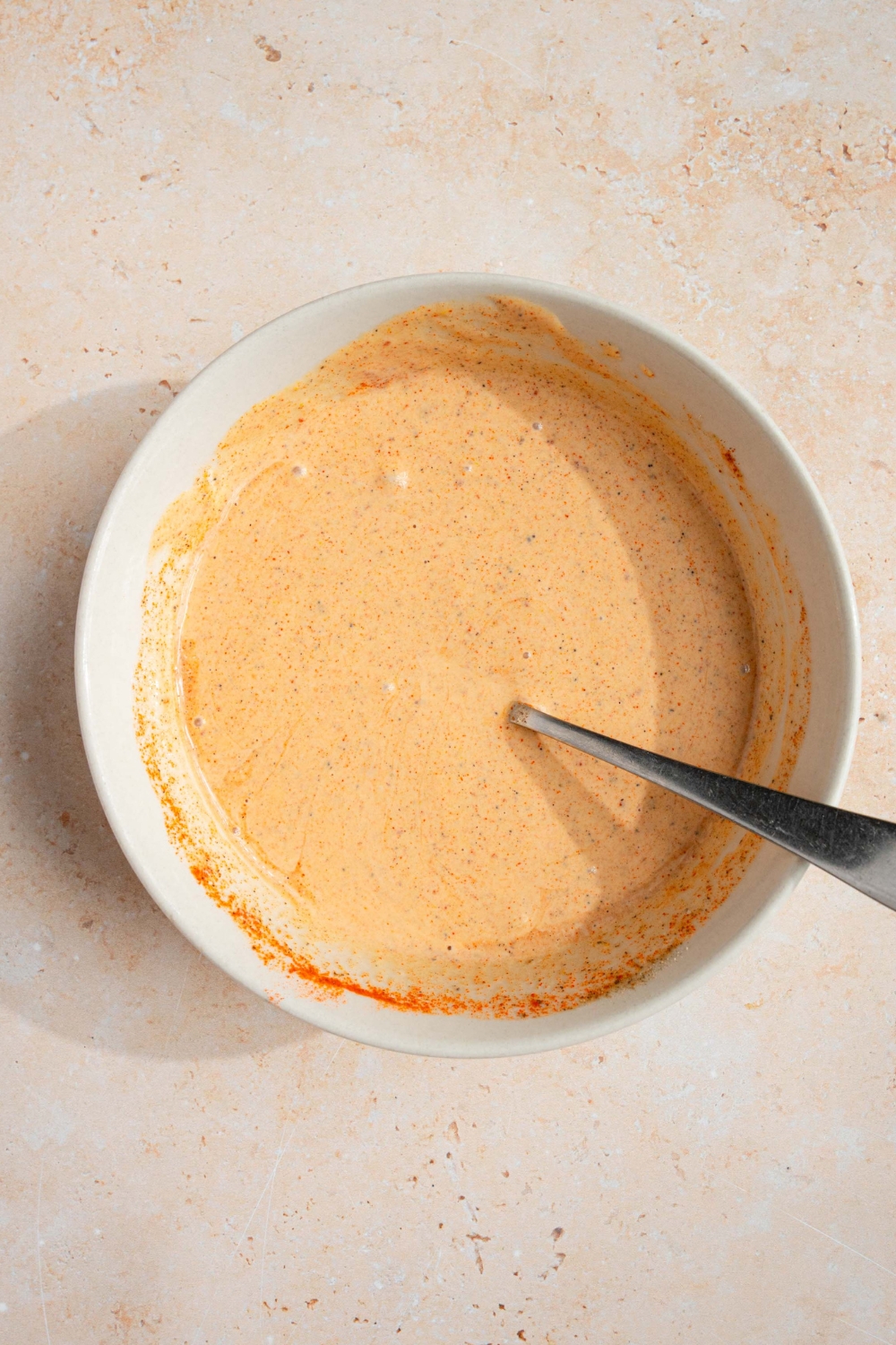 A spoon submerged in a white bowl of smash burger taco sauce.