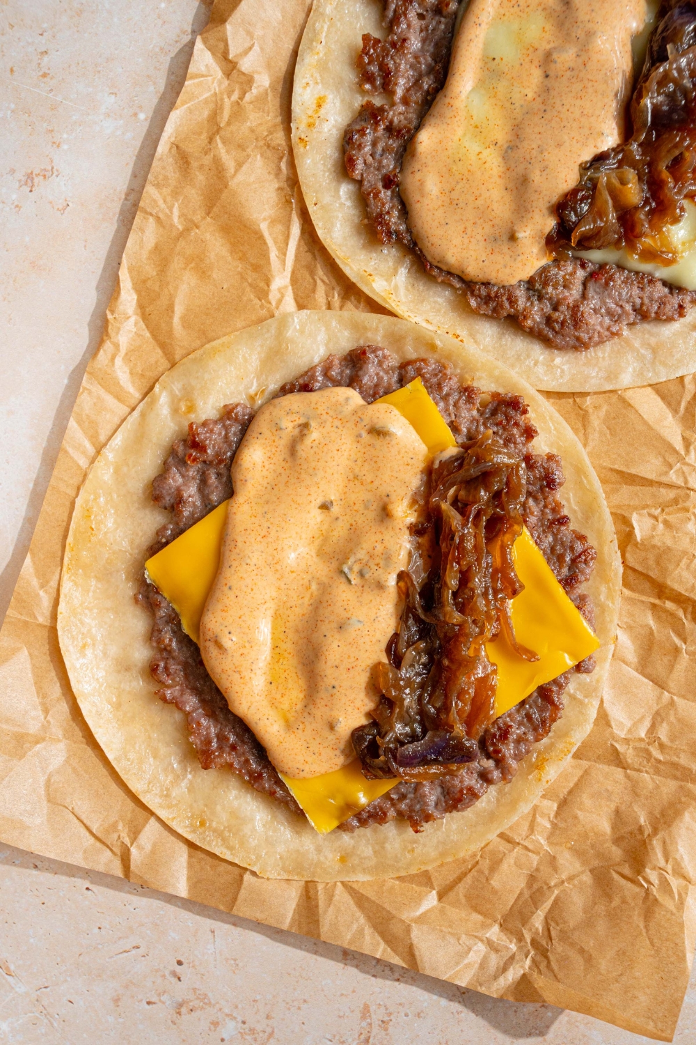 Smash burger sauce on top of cheddar cheese on a smash burger in a tortilla on a sheet of parchment paper.