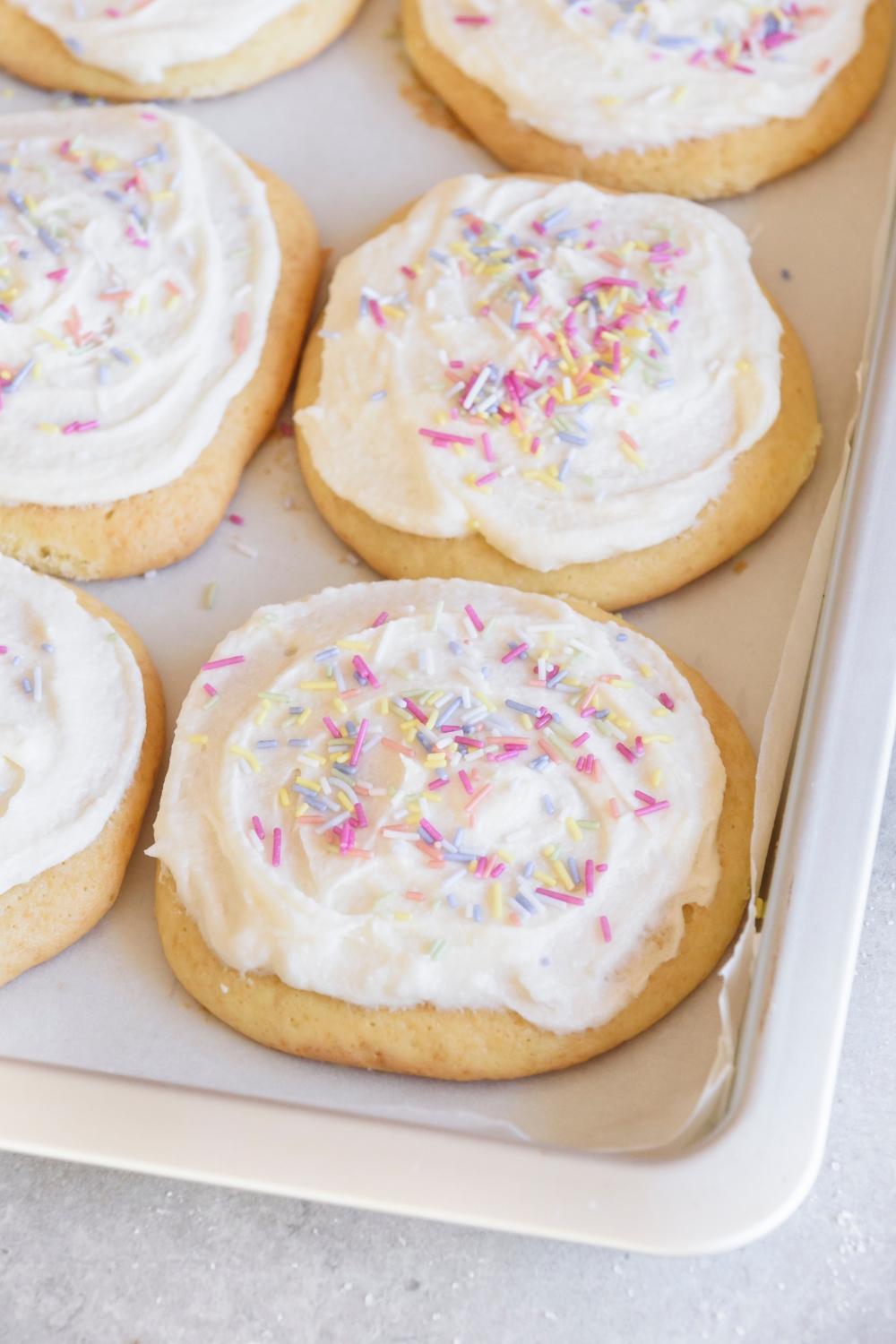 A baking sheet with bakes sugar cookies that are frosted and topped with sprinkles.