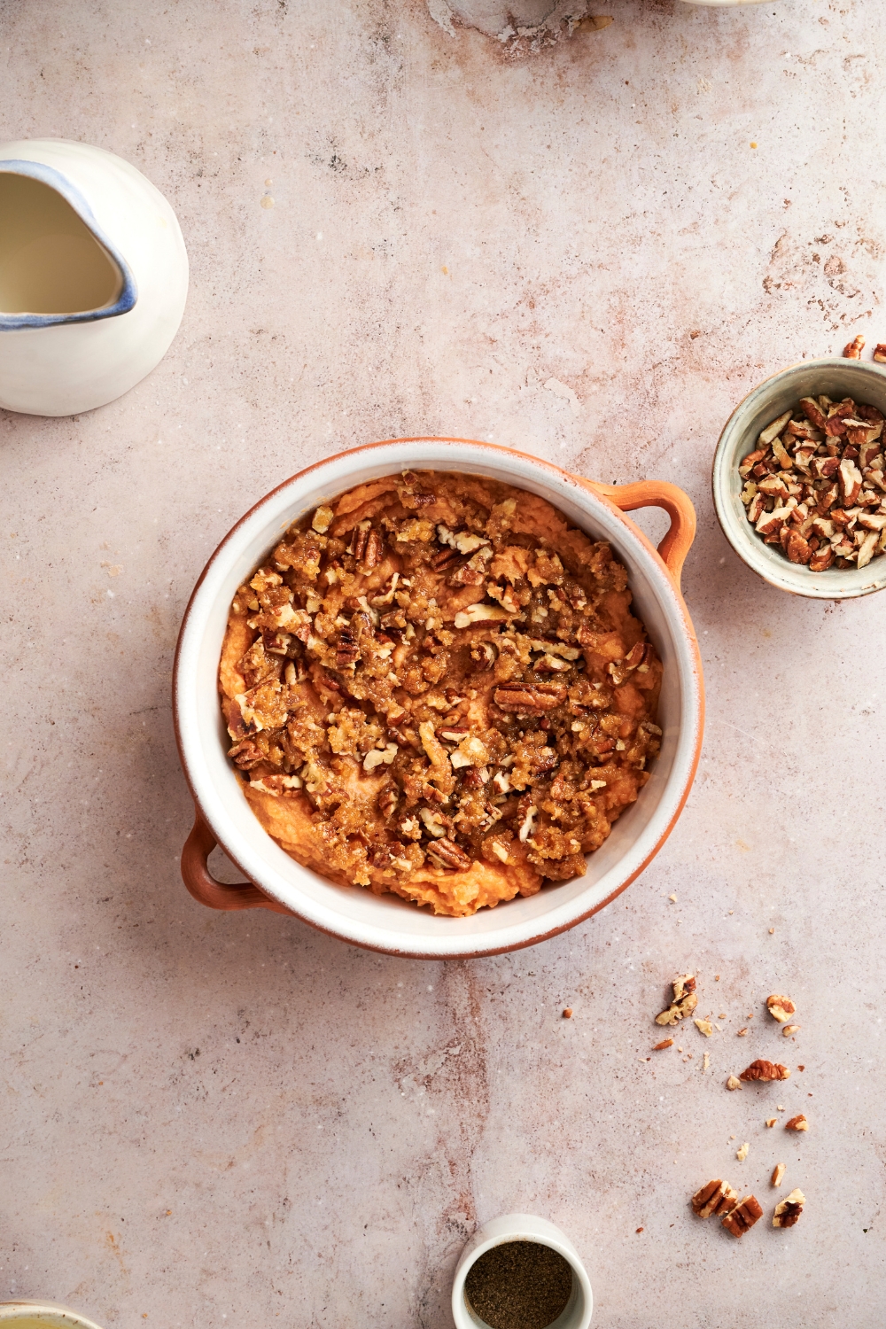 A white pot full of sweet potato casserole is on a gray counter. The casserole is topped with golden brown pecan topping.