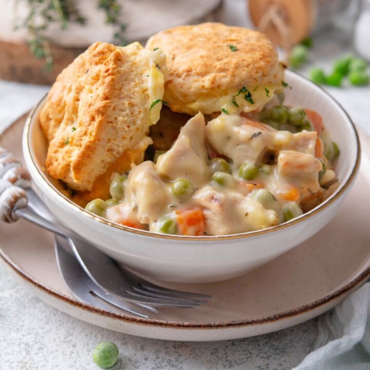 Turkey pot pie and two biscuits in a bowl that is on a plate with two forks on top of a grey counter.
