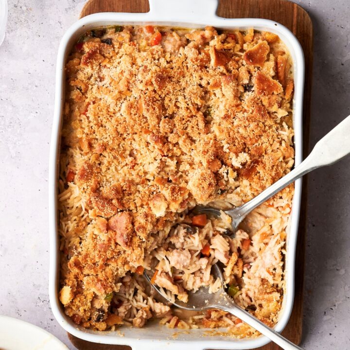 Ritz crackers on top of turkey rice casserole in a white casserole dish on top of a wooden cutting board.