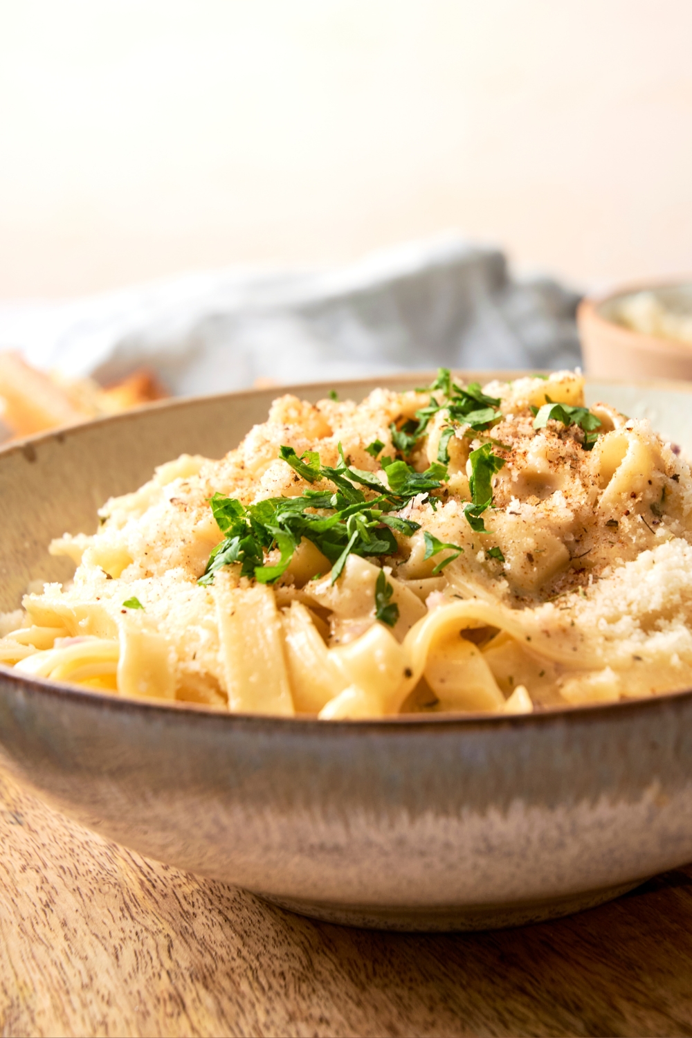 A large white bowl is piled high with fettuccine and Cajun alfredo sauce. It is topped with extra cheese, fresh herbs, and Cajun seasoning.
