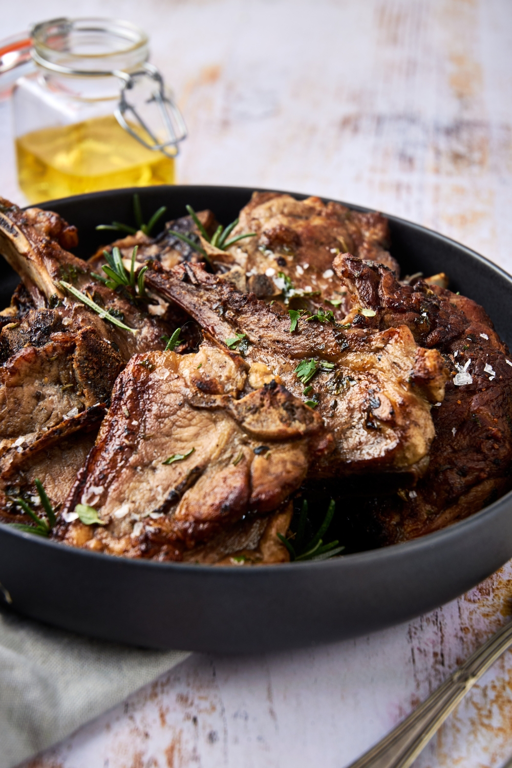 A black dish is full of lamb shoulder chops garnished with fresh parsley and sea salt.